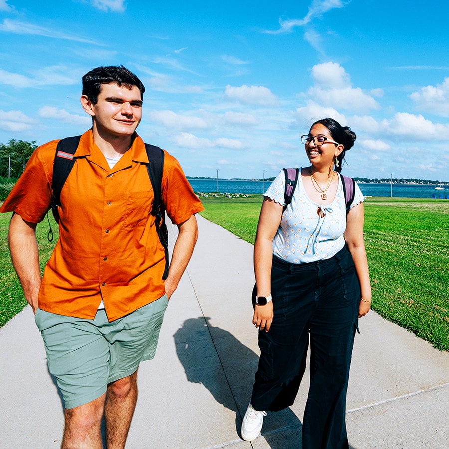 Two students talk while walking by the harbor on a sunny day at UMass Boston