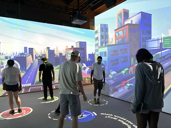 5 students exlporing a virtual relatily game at the museum of science with cityscapes in the background