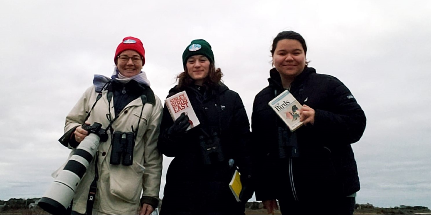 three birders standing and smiling with bird guides and gear