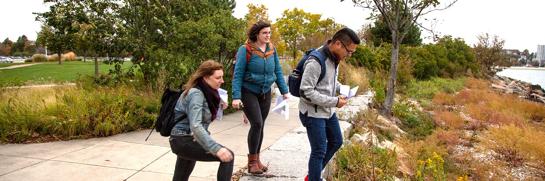 3 students work at Carson Beach doing outdoor research with clipboards.
